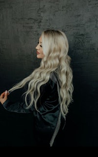 a blonde woman with long wavy hair posing against a black wall